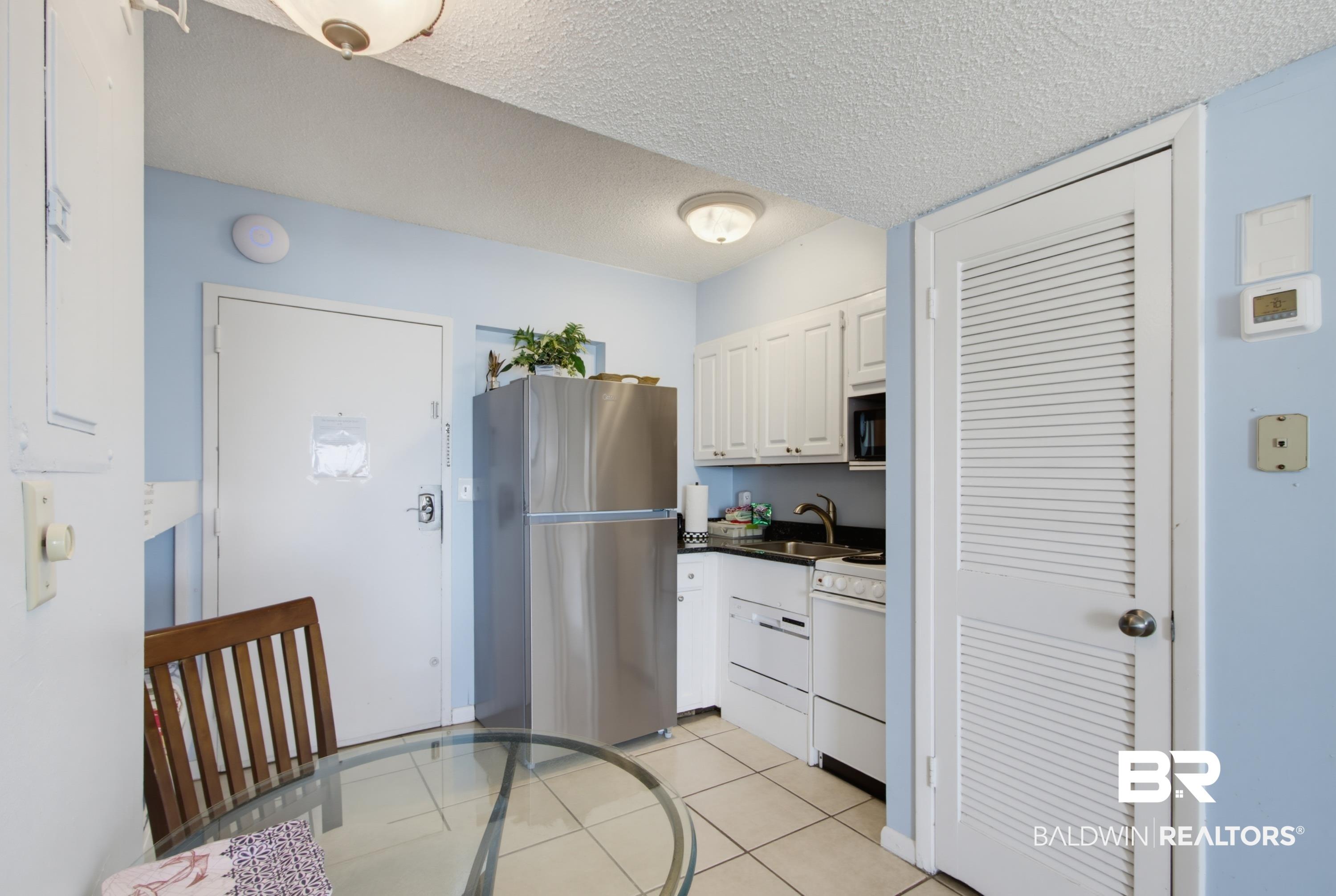 Image 4: Compact kitchen featuring white cabinetry, dark countertops, and stainless steel refrigerator