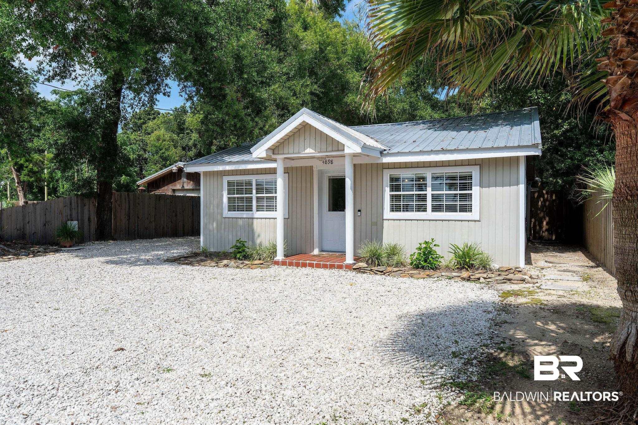 Image 2: Single-story residence featuring a gray metal roof and light-colored vertical siding