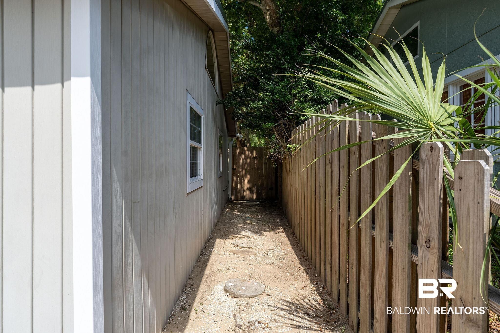 Image 3: Board and batten siding with white-trimmed windows, a wooden picket fence, and established palm foliage