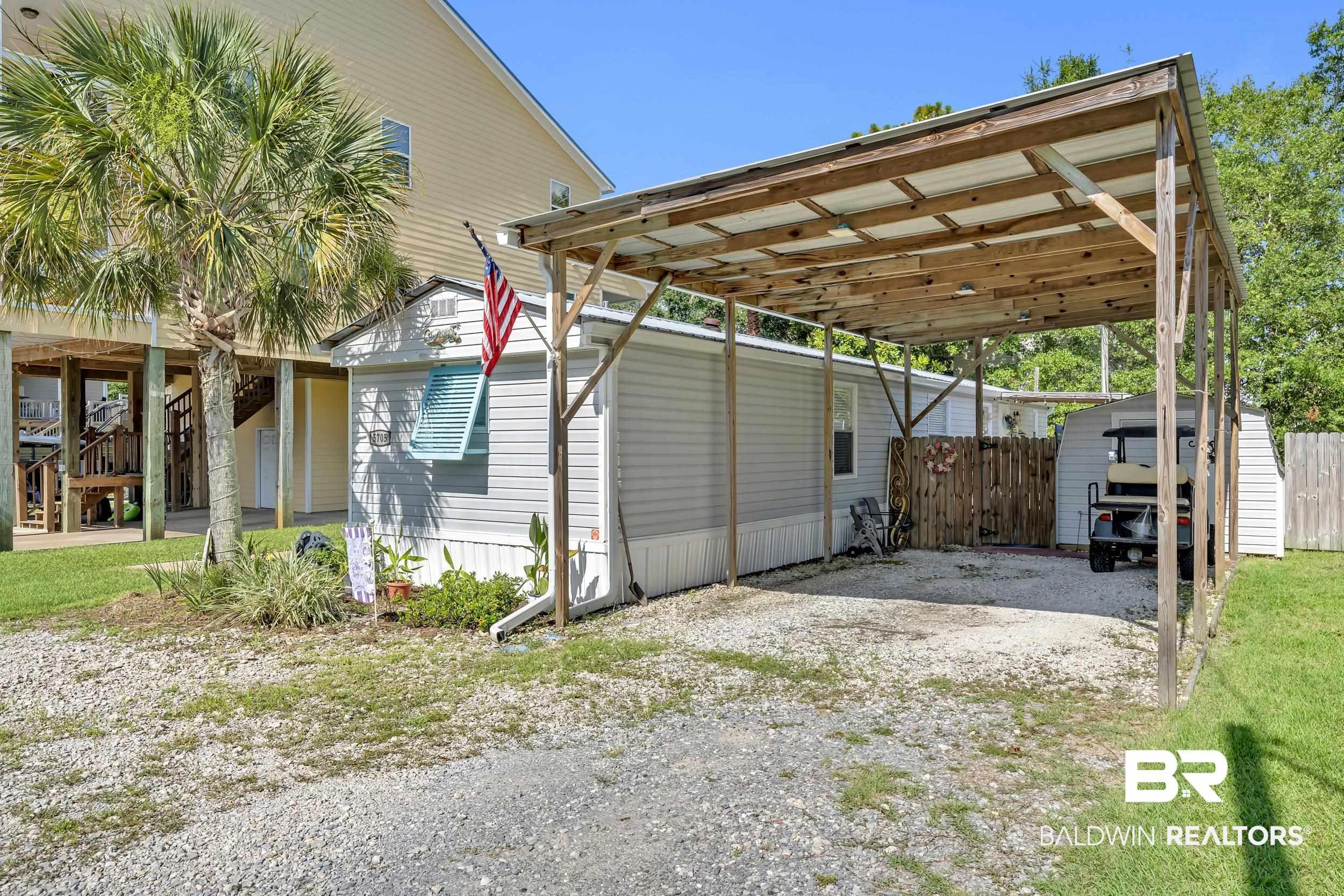 Image 4: Gravel parking area featuring a carport, an exterior storage shed, and mature palm tree