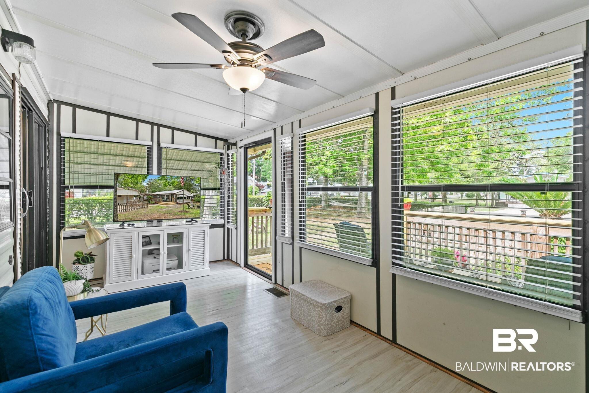 Image 3: Enclosed sunroom featuring wood-finish flooring, a ceiling fan with integrated lighting, and multiple windows with horizontal blinds