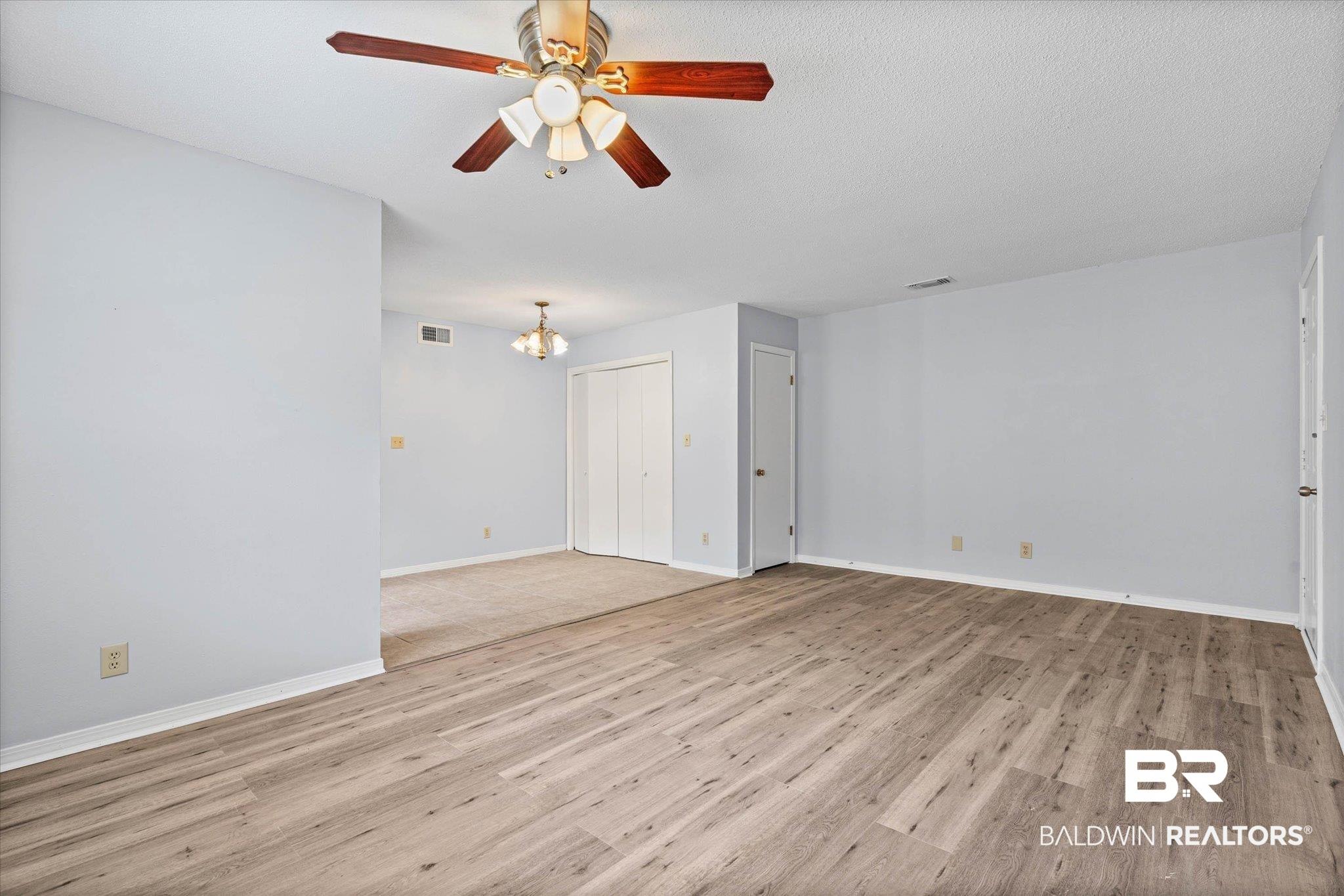 Image 4: Open-concept living area featuring wood-finish flooring, a ceiling fan with light kit, and neutral wall tones