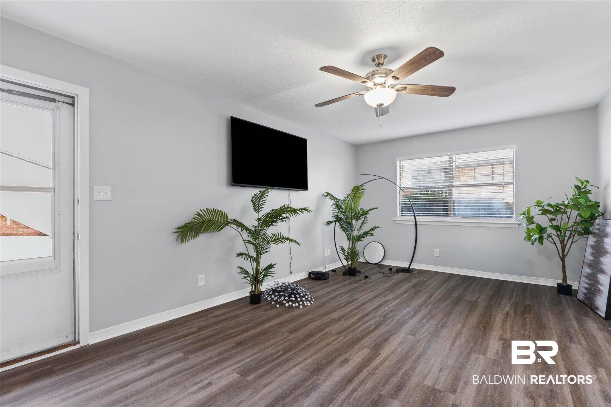 Image 3: Spacious living area featuring wood-finish flooring, light gray wall paint, and a ceiling fan with integrated lighting