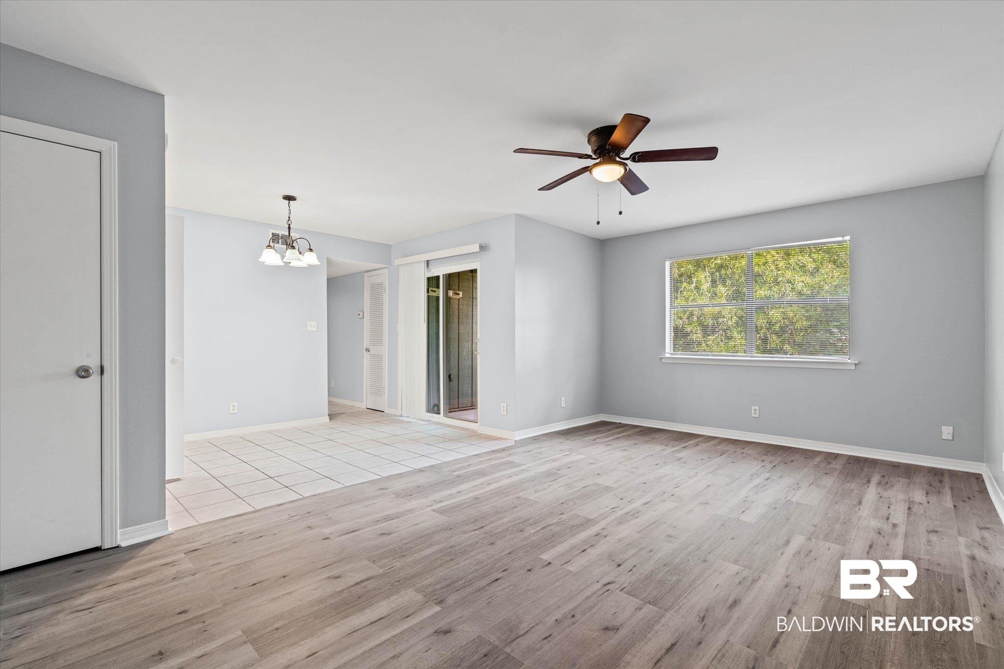 Image 3: Open living space featuring wood-finish flooring, a ceiling fan with integrated lighting, and a large window