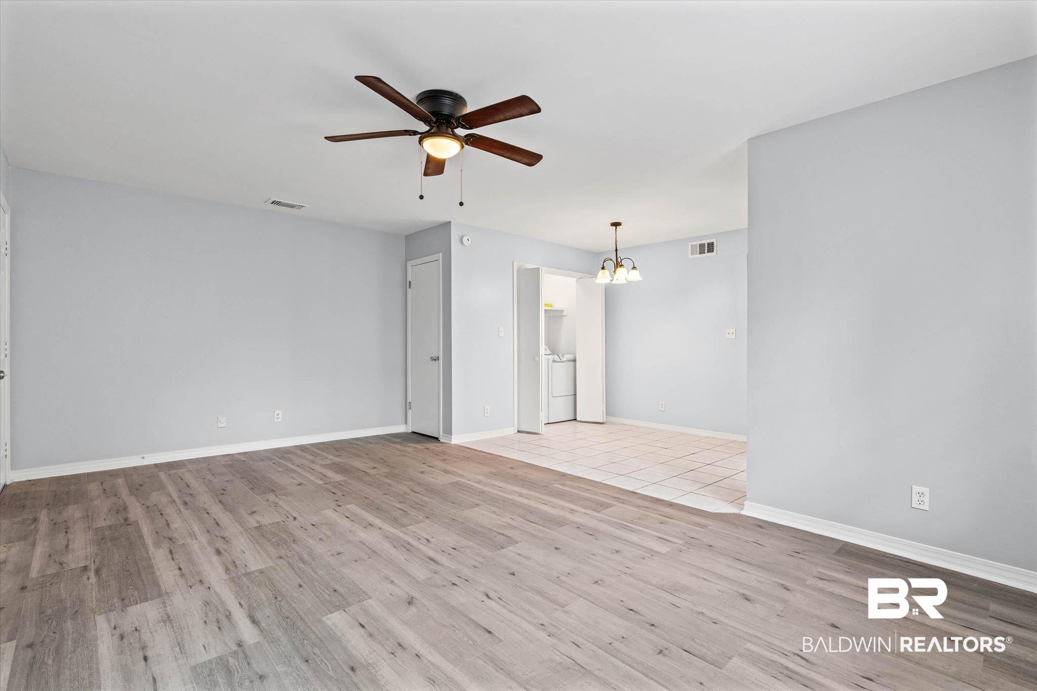 Image 4: Spacious room with wood-finish flooring, light gray walls, and a ceiling fan with integrated lighting