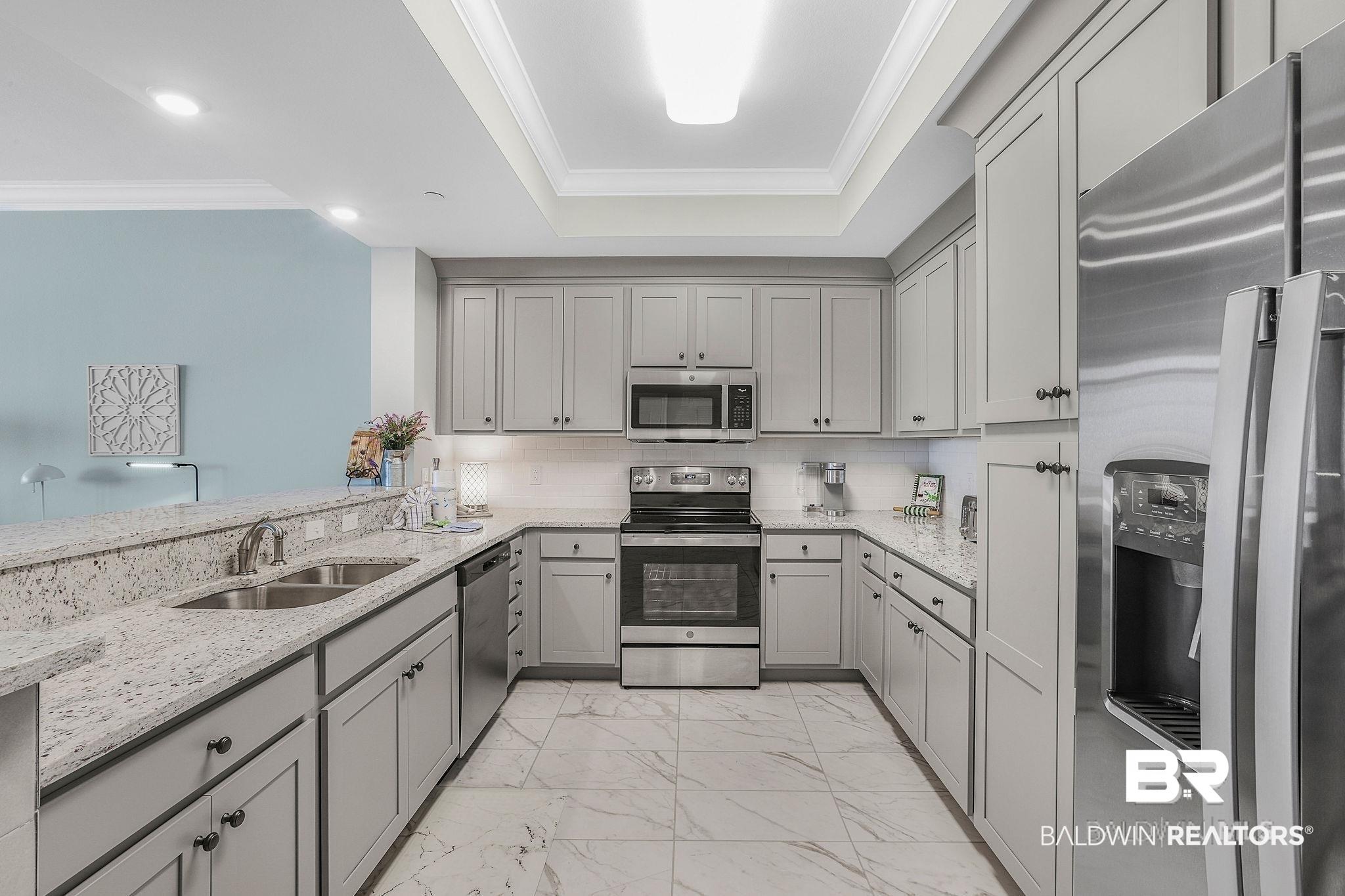 Image 2: U-shaped kitchen featuring light gray cabinetry with dark hardware, stainless steel appliances, a tile backsplash, and light-toned, speckled countertops