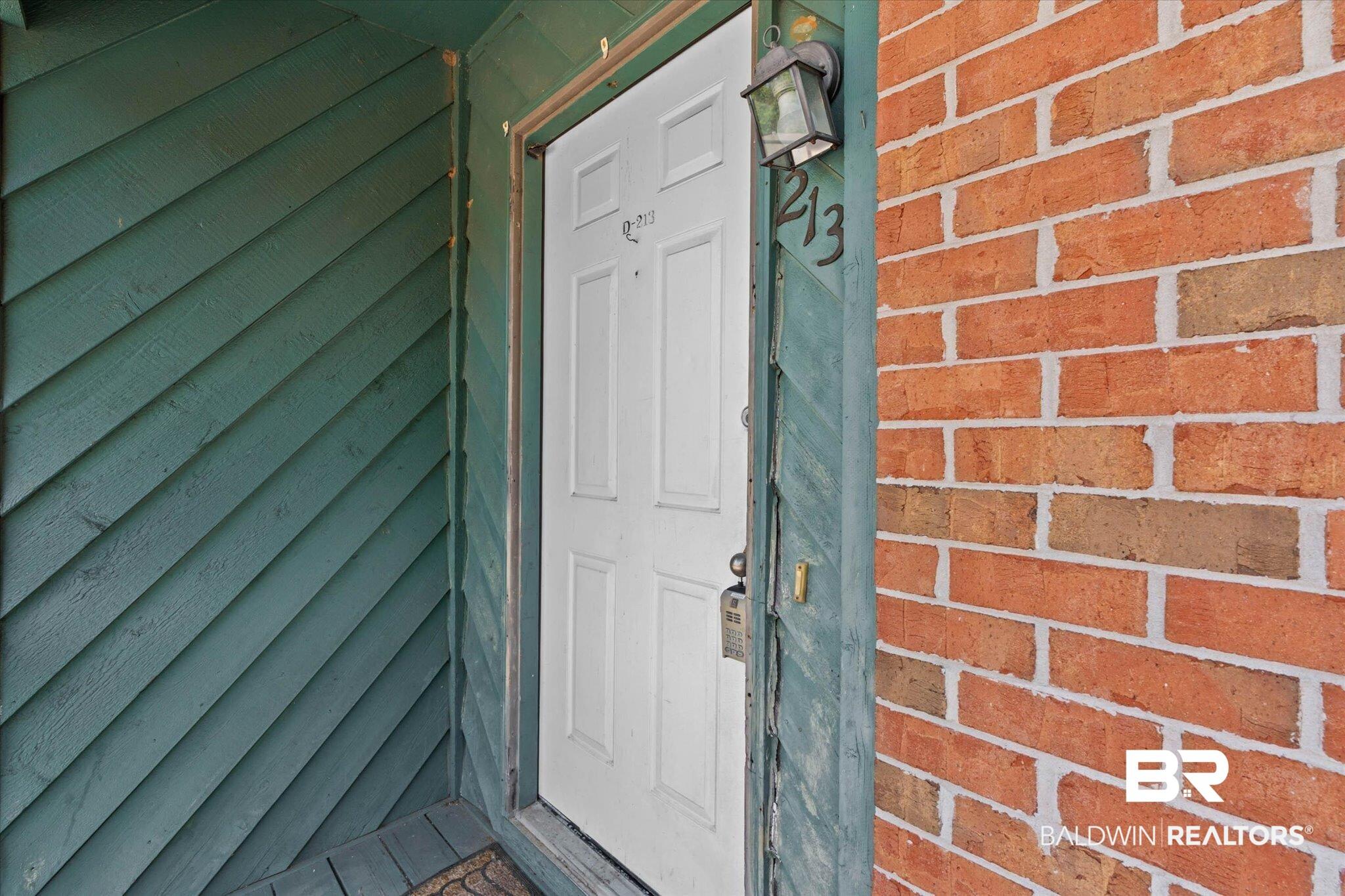 Image 2: Entryway featuring a white paneled door, brick exterior, and diagonal wood siding