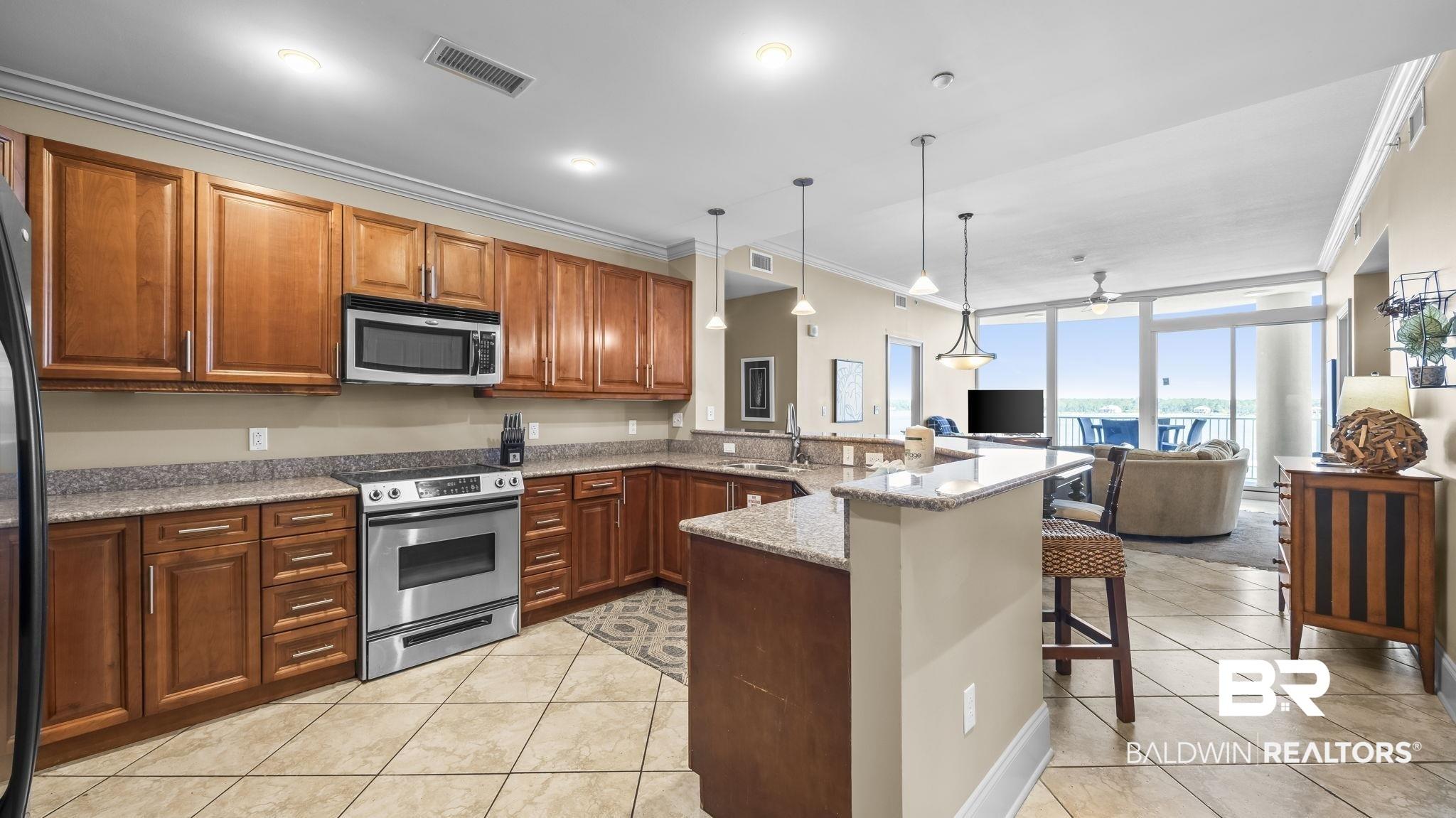 Image 2: Open-concept kitchen featuring wood cabinetry, stainless steel appliances, granite countertops, and tile flooring