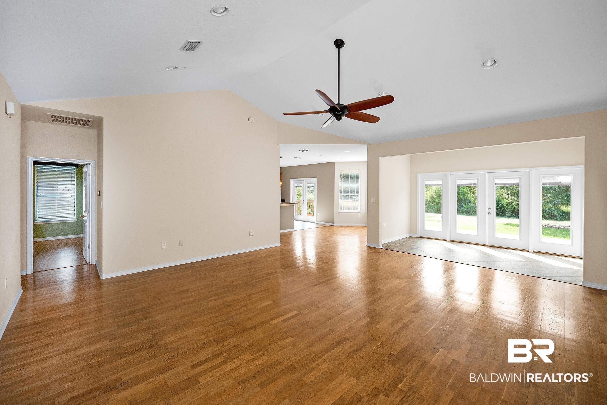 Image 2: Spacious living area featuring wood-finish flooring, a vaulted ceiling, and a ceiling fan