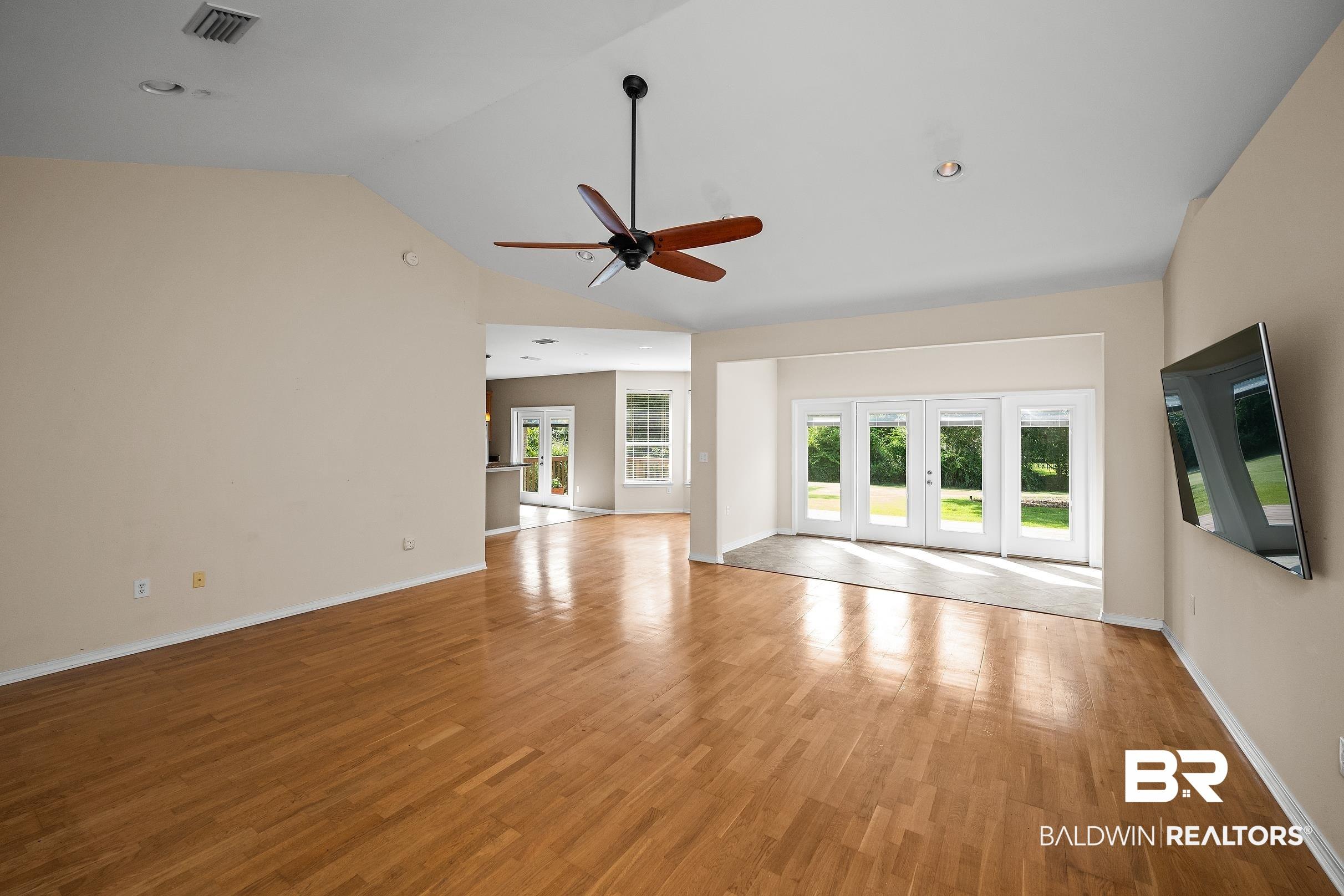 Image 3: Spacious interior featuring wood-finish flooring, vaulted ceilings, and a ceiling fan