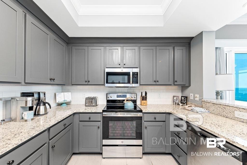 Image 3: U-shaped kitchen featuring extensive light-toned countertops, gray cabinetry, and a white subway tile backsplash