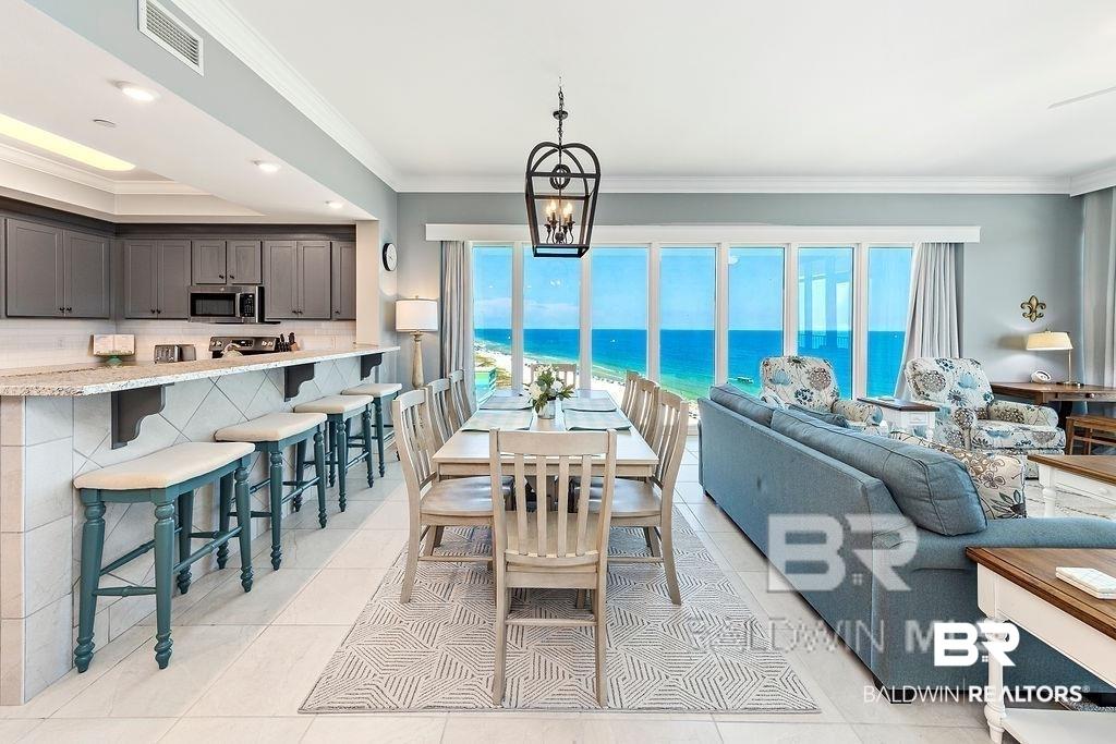 Image 4: Open-concept living area featuring a full wall of floor-to-ceiling windows, light-toned tile flooring, and a dining area with an overhead chandelier