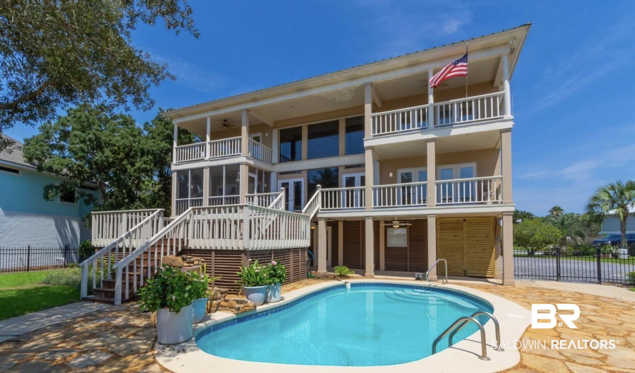 Image 2: Multi-level residence featuring an inground swimming pool with stone surround, a screened porch, and multiple balconies with white railings