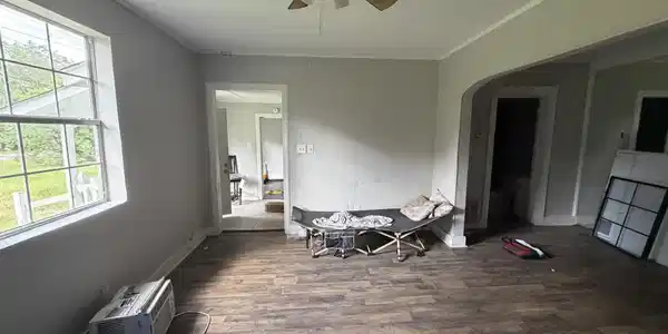 Image 2: Spacious interior room featuring wood-finish flooring, a ceiling fan, and ample natural light from a multi-pane window