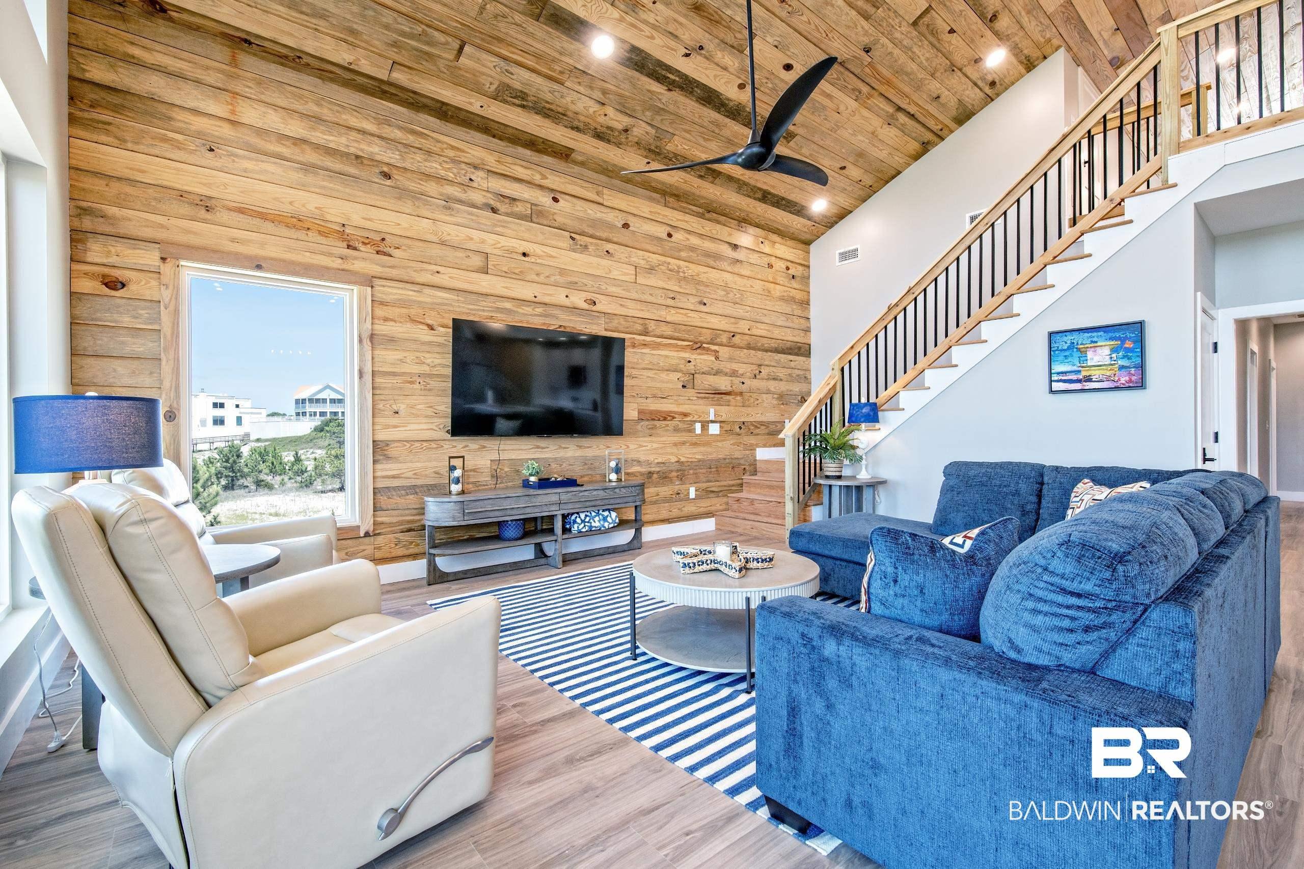 Image 4: Vaulted ceiling with wood-finish planks, accent wall featuring horizontal wood paneling, open staircase with wood handrails and black balusters, recessed lighting, and wood-finish flooring