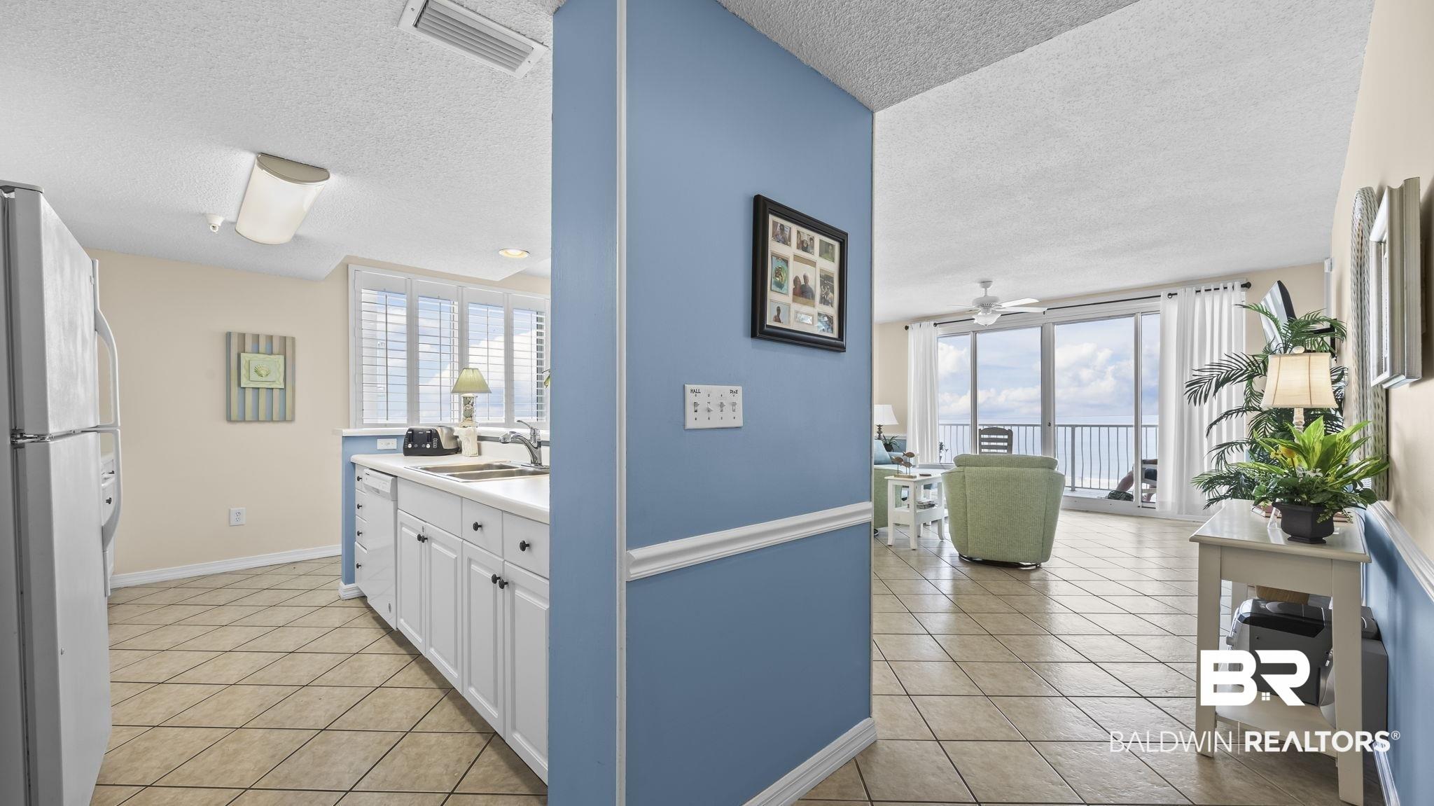 Image 2: Open-concept living space with tile flooring throughout, featuring a kitchen with white cabinetry and a living area with sliding glass doors opening to a balcony