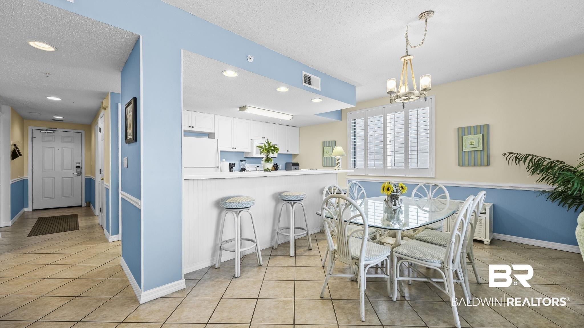 Image 3: Open-concept kitchen and dining area featuring white cabinetry, a breakfast bar with beadboard paneling, and tile flooring