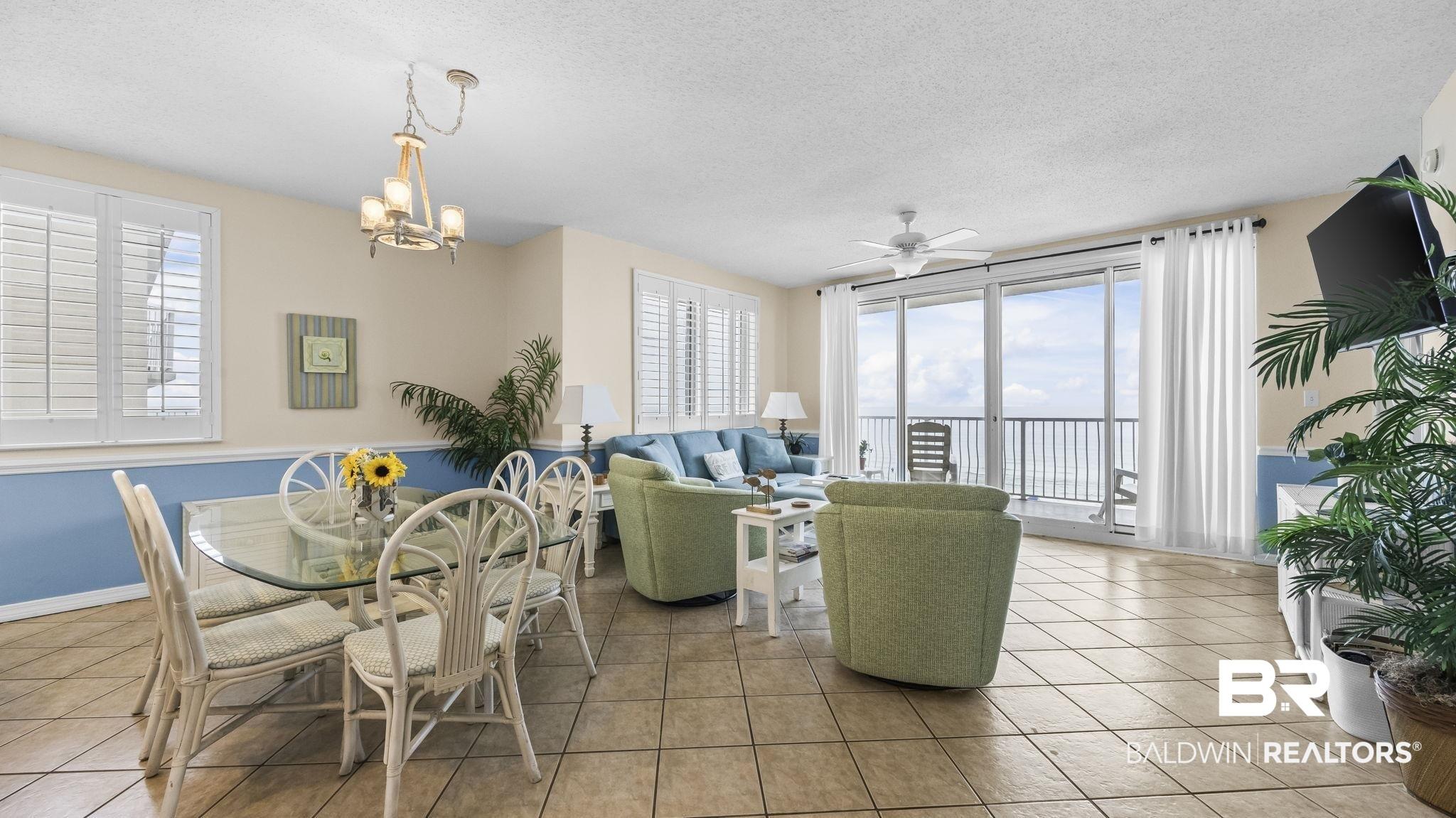 Image 4: Open-concept living area with tile flooring throughout, featuring a dining space with a chandelier and plantation shutters