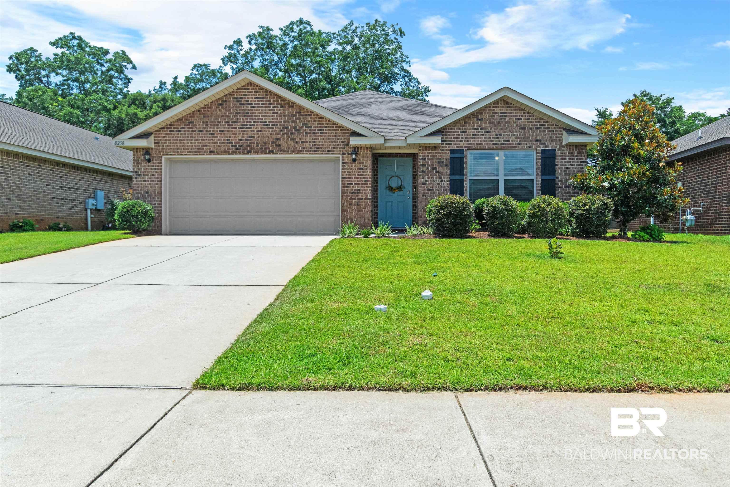 Image 2: Brick facade residence featuring an attached garage with a paved driveway, a manicured front lawn, and mature landscaping