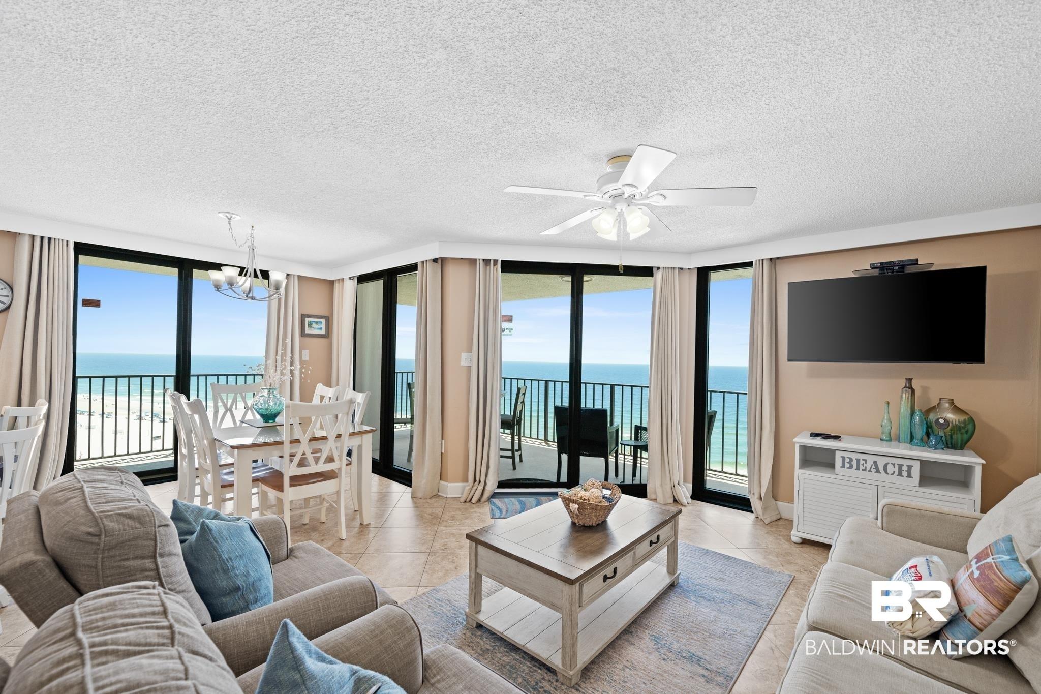 Image 2: Expansive living area with tile flooring, featuring floor-to-ceiling glass doors and windows showcasing direct ocean and beach panoramas