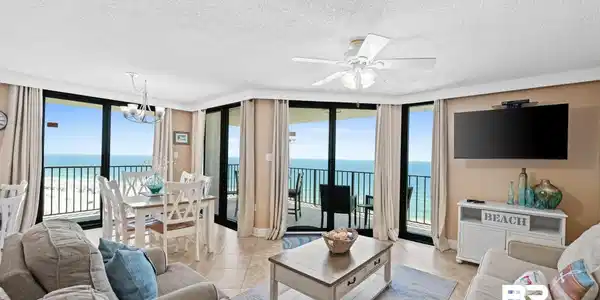 Image 2: Expansive living area with tile flooring, featuring floor-to-ceiling glass doors and windows showcasing direct ocean and beach panoramas