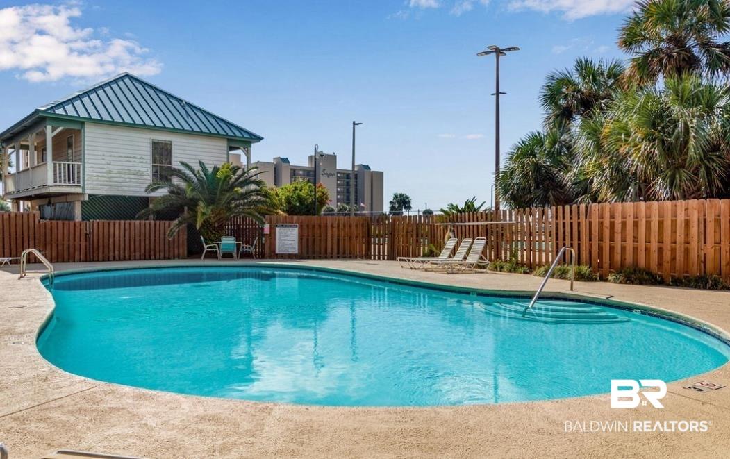 Image 4: Curved swimming pool with integrated steps, surrounded by concrete decking and a wooden privacy fence
