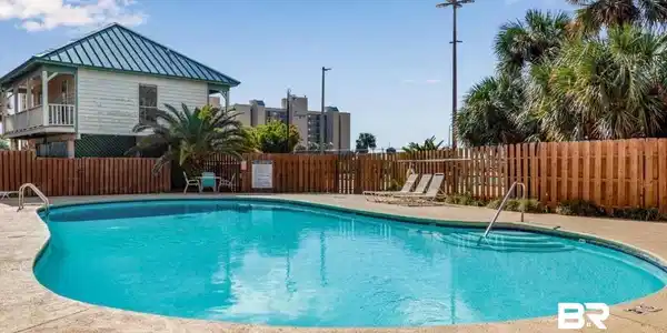 Image 4: Curved swimming pool with integrated steps, surrounded by concrete decking and a wooden privacy fence