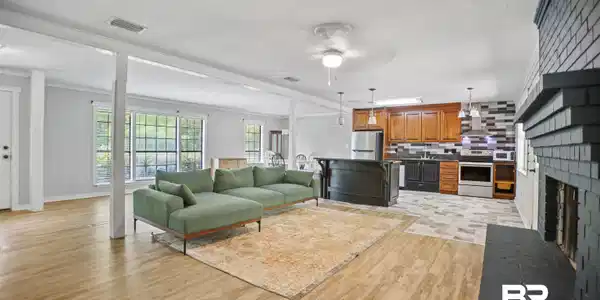 Image 3: Expansive open-concept living area featuring light wood-finish flooring, a painted brick fireplace, and large windows