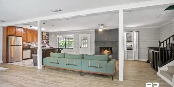 Image 4: Spacious living area featuring wood-finish flooring, a contemporary gray brick fireplace, and shiplap accent walls