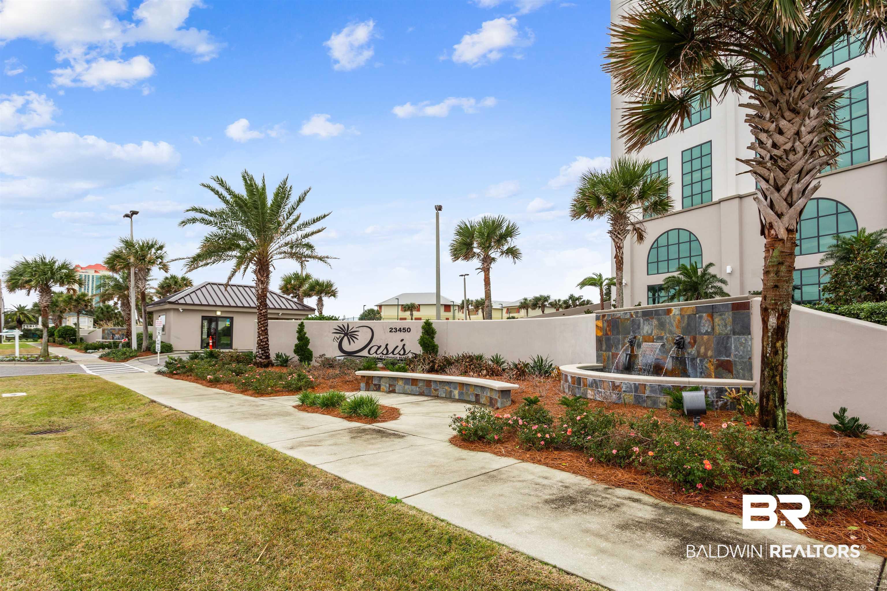 Image 3: Property entrance featuring a stone-clad fountain, stone benches, palm trees, and a decorative sign