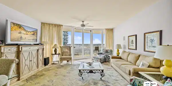 Image 2: Spacious living area featuring large sliding glass doors, balcony access, a ceiling fan, light-toned walls, and decorative wall art