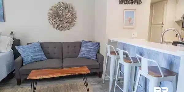 Image 4: Open-concept living space featuring a breakfast bar with seating for three, a stainless steel sink with gooseneck faucet, and light-toned flooring