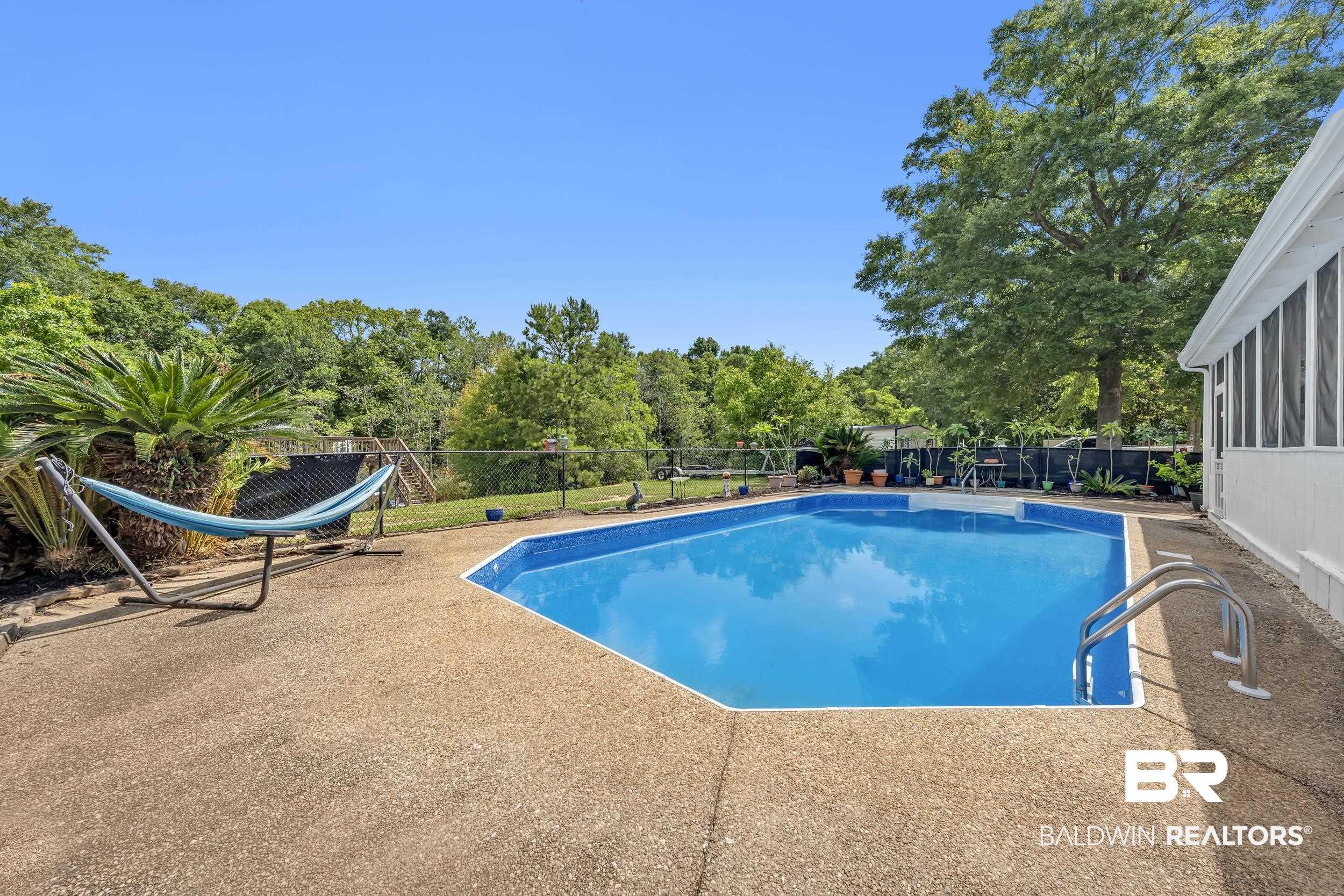 Image 3: In-ground swimming pool with an irregular shape and integrated steps, surrounded by an exposed aggregate concrete patio