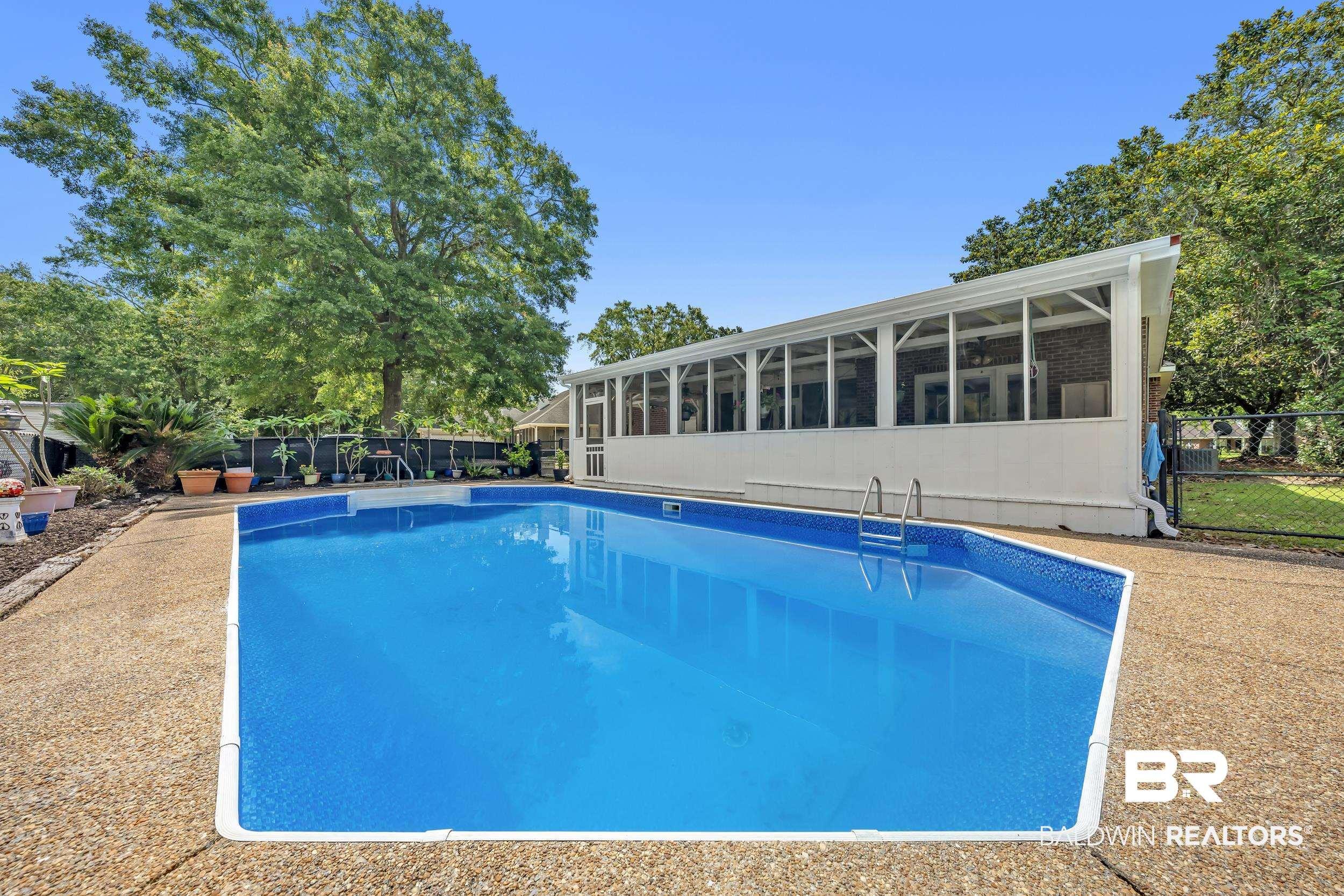 Image 4: In-ground swimming pool with an adjacent screened patio featuring multiple windows and a white exterior finish