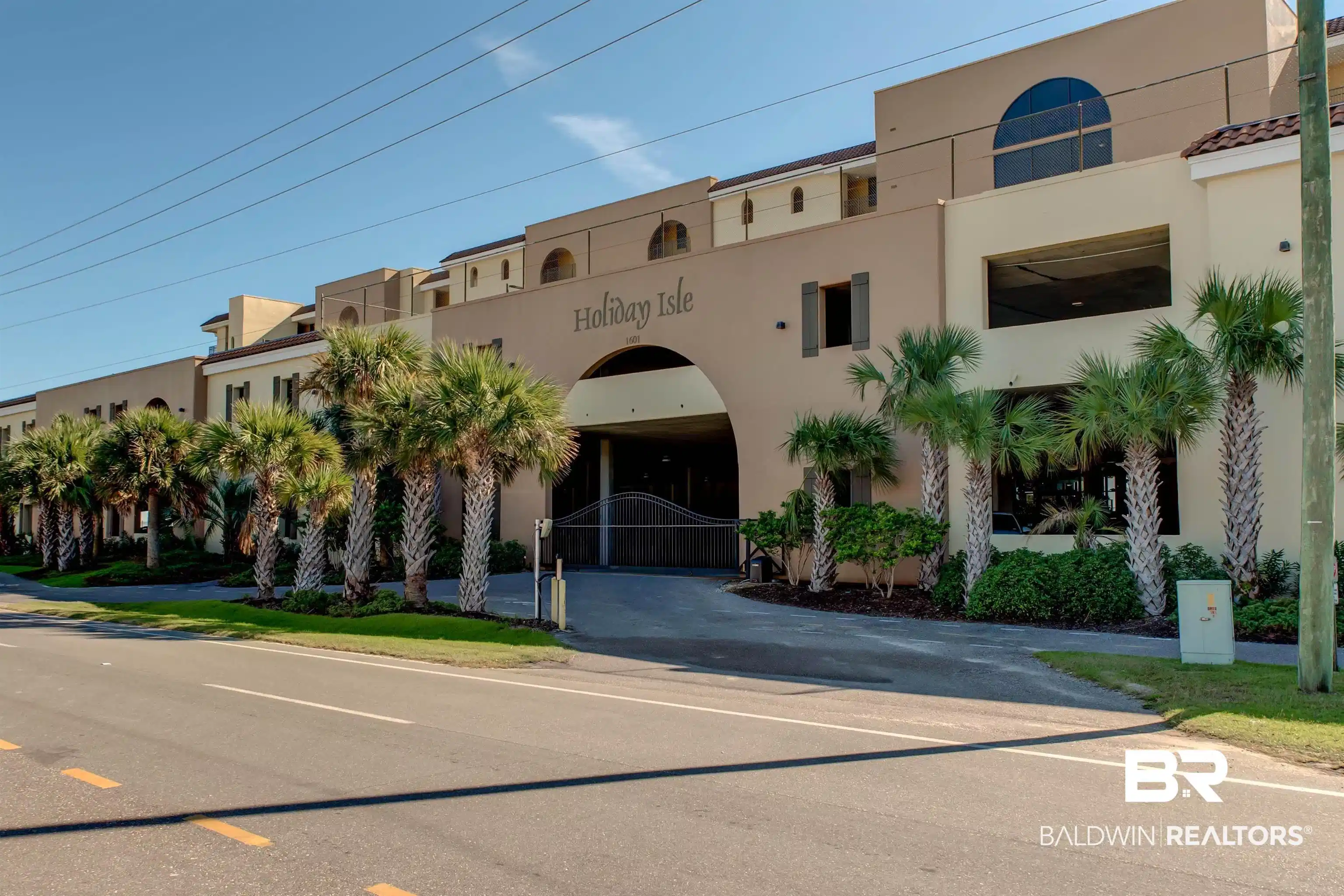 Image 1: Mediterranean-inspired multi-story building featuring a prominent arched entryway, a row of mature palm trees, stucco exterior, and terracotta-style roof tiles