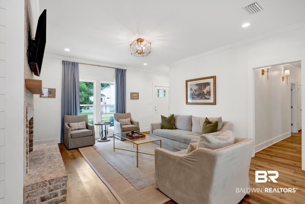 Image 4: Spacious living area featuring wood-finish flooring, a brick fireplace with a wood mantle, and crown molding