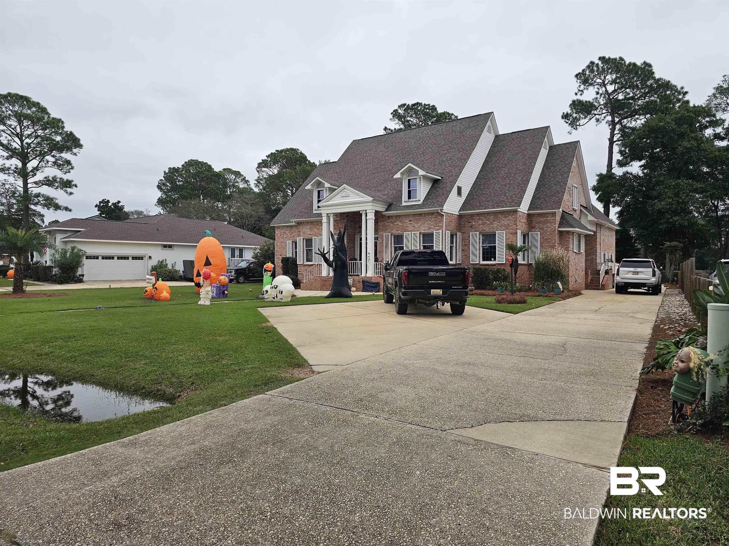 Image 1: Traditional brick home featuring a prominent portico entrance with white columns, a shingled roof with multiple gables, white window shutters, and a concrete driveway