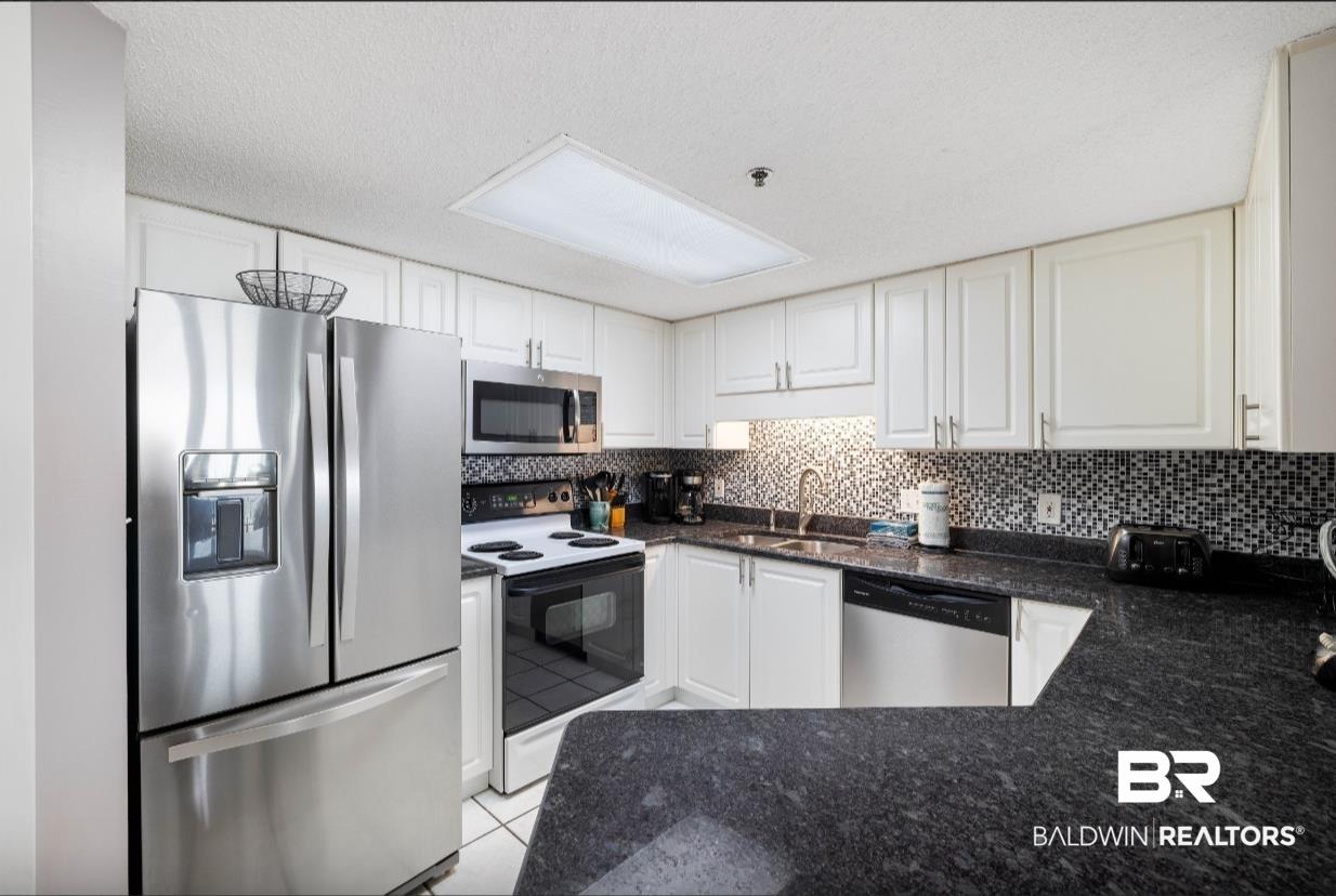 Image 4: Kitchen featuring white cabinetry, dark speckled countertops, stainless steel appliances, and a mosaic tile backsplash