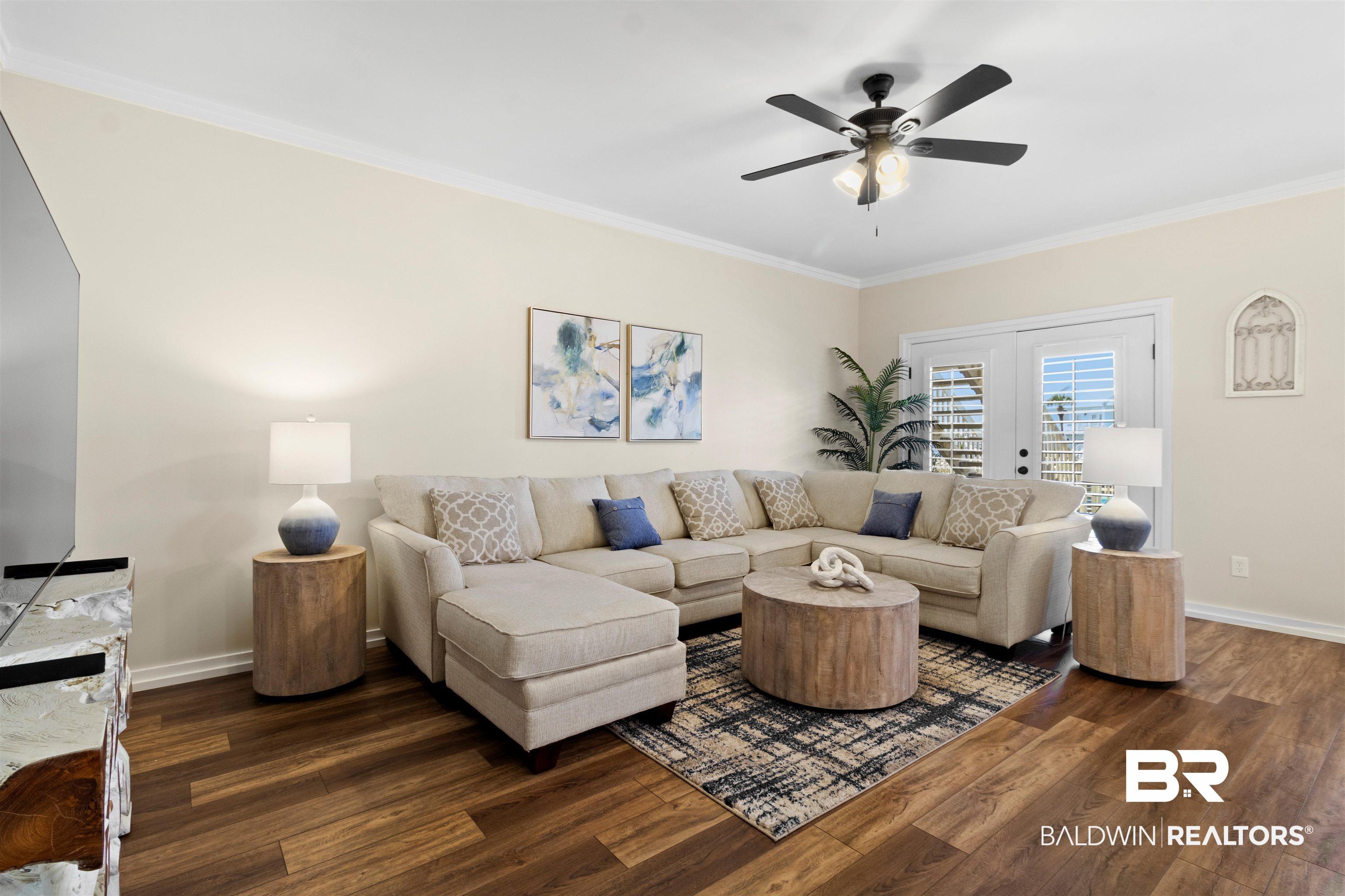 Image 2: Spacious living area featuring wood-finish flooring, crisp white baseboards, and crown molding