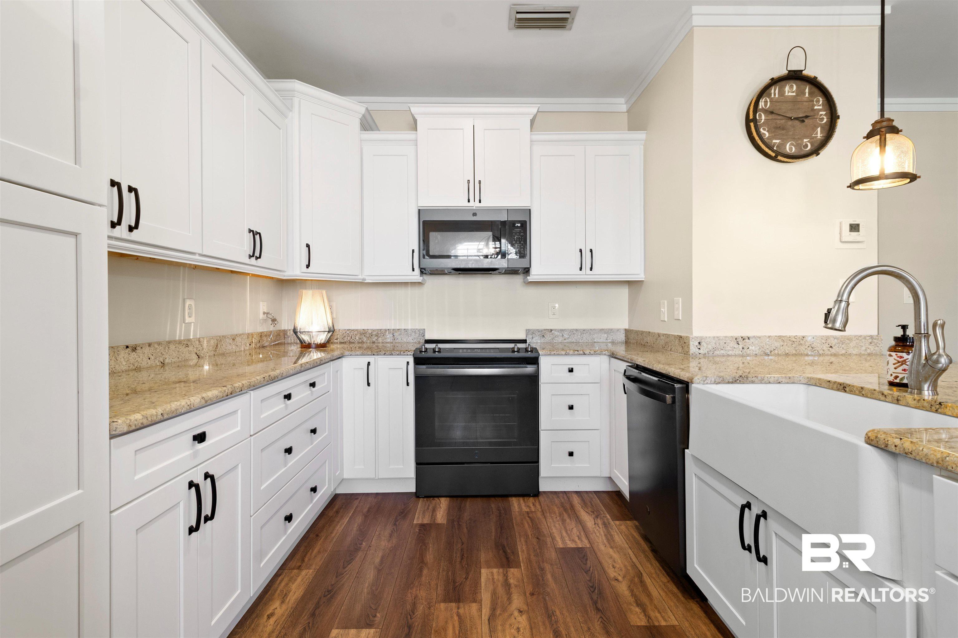Image 3: Kitchen featuring white shaker cabinetry, speckled stone countertops, wood-finish flooring, a white farmhouse sink, and black appliances
