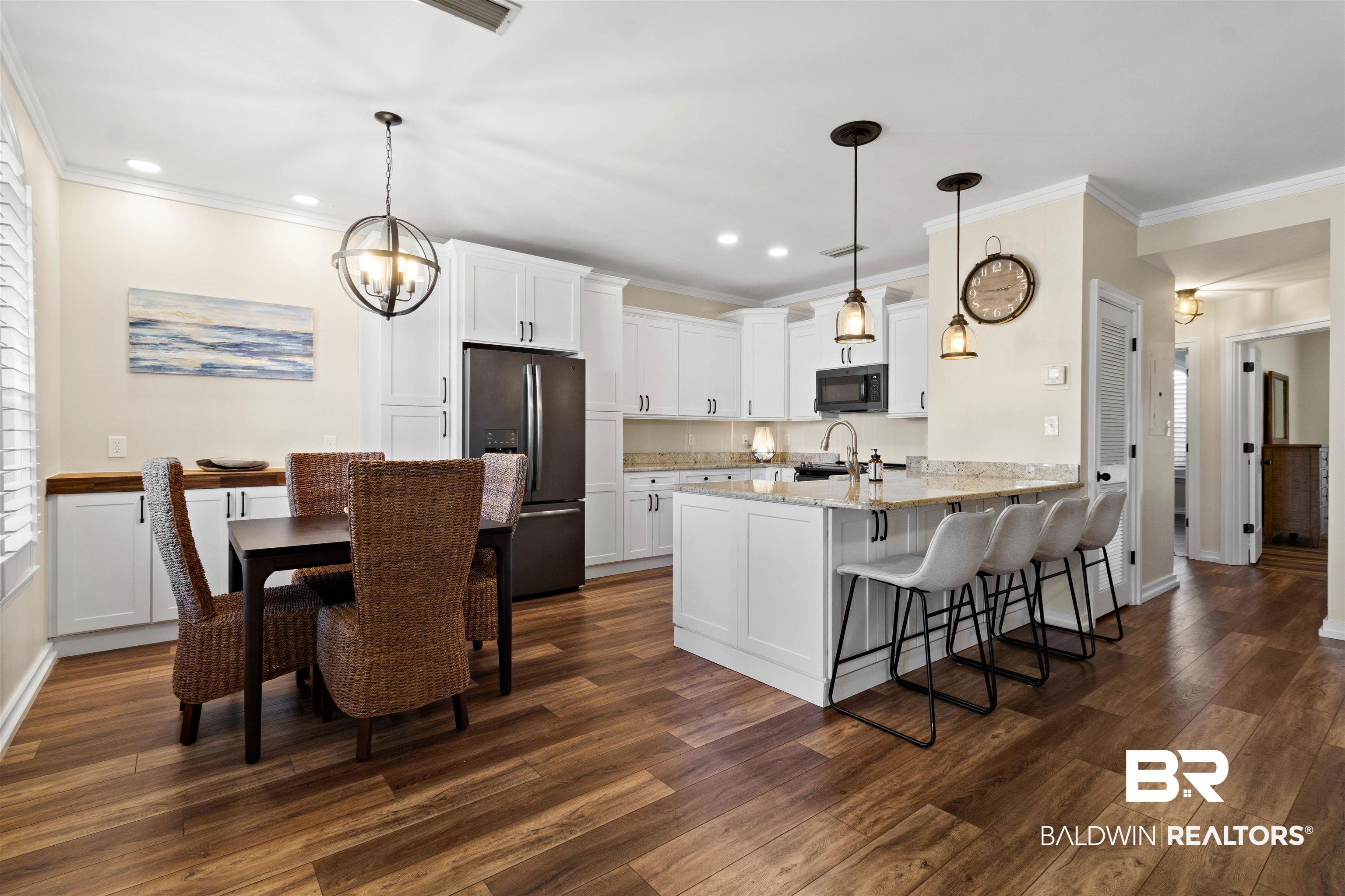 Image 4: Open-concept kitchen and dining area featuring wood-finish flooring, white cabinetry, a kitchen island with granite countertop, and integrated stainless steel appliances