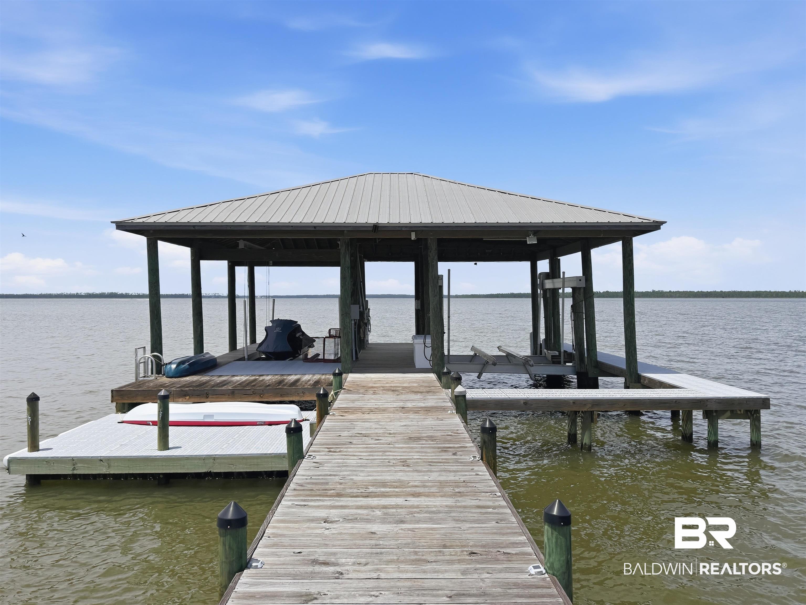 Image 3: Covered boat dock featuring a metal roof, boat lift, and an expansive pier leading to the water