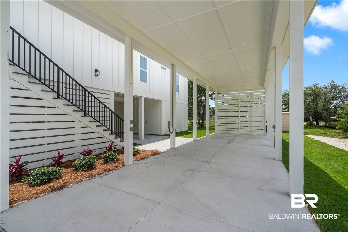 Image 4: Covered concrete area featuring a large open space, exterior staircase with black metal railing, and white wood-plank siding