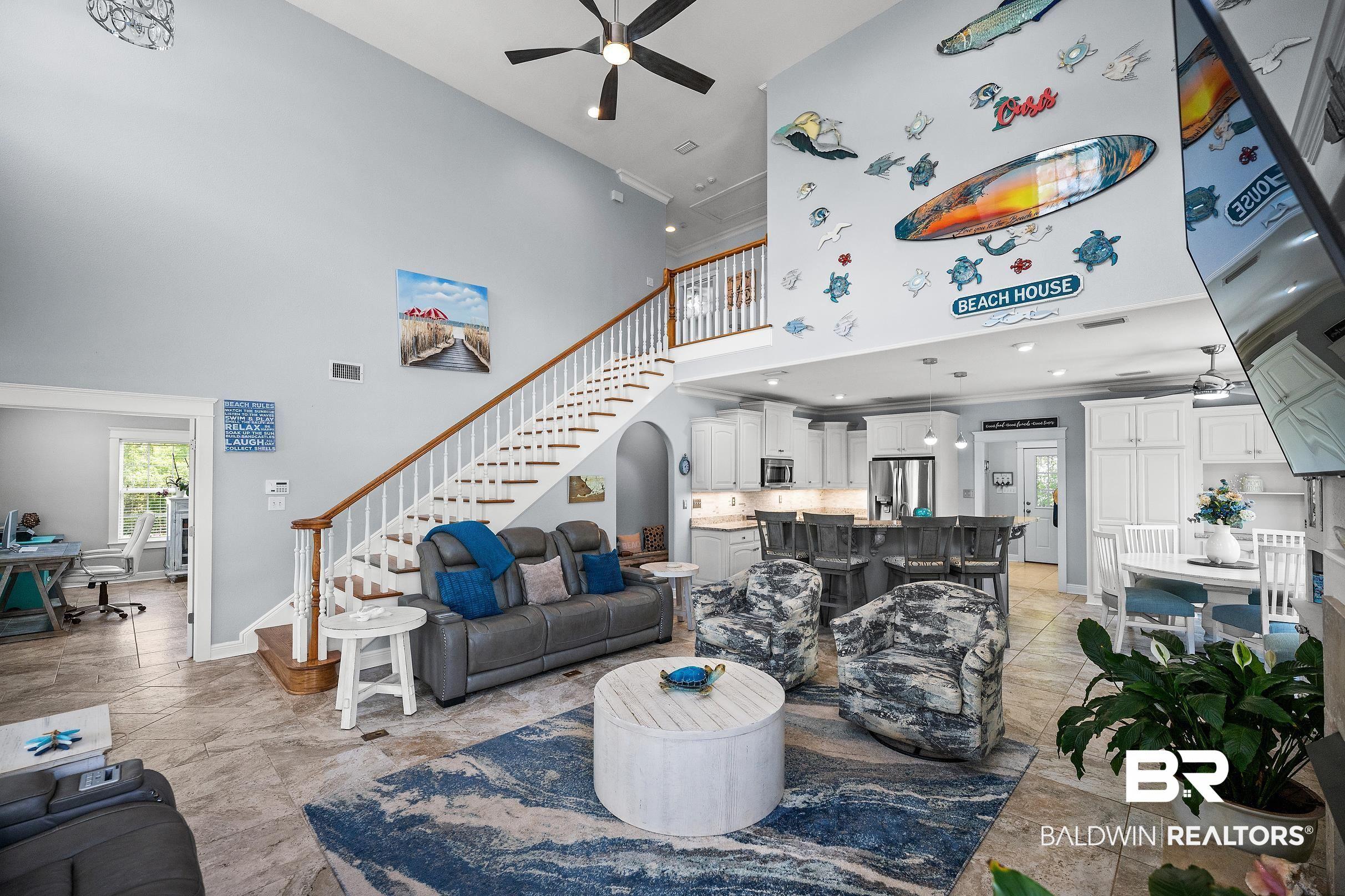 Image 3: Two-story living area featuring vaulted ceilings, a prominent staircase with wood railing, tile flooring, and an open-concept layout connecting to a kitchen with a central island