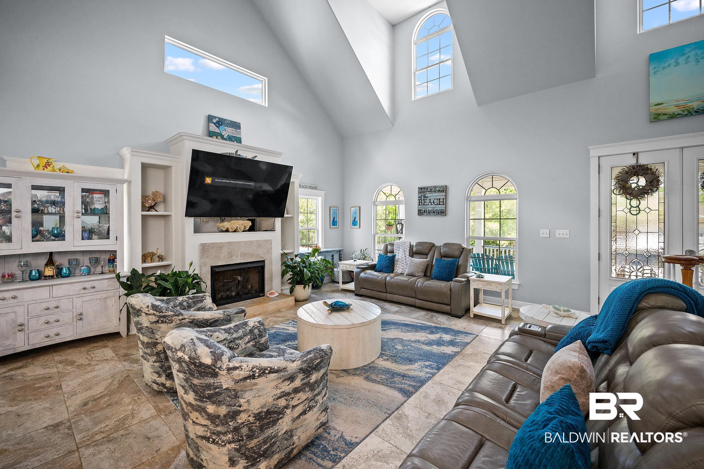 Image 4: Vaulted ceiling living area featuring a built-in fireplace with a hearth, custom cabinetry with glass-front uppers, arched windows, transom windows, and tiled flooring