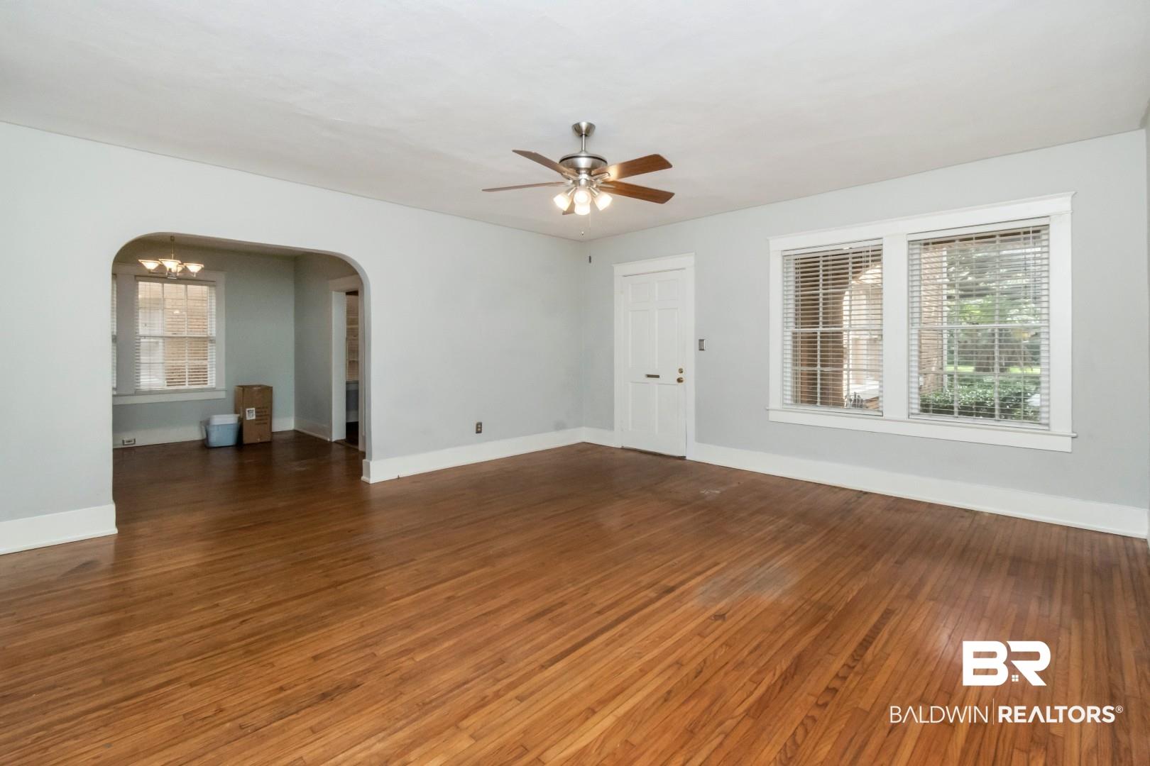 Image 4: Empty room with dark wood-type flooring, a chandelier, arched walkways, and ceiling fan