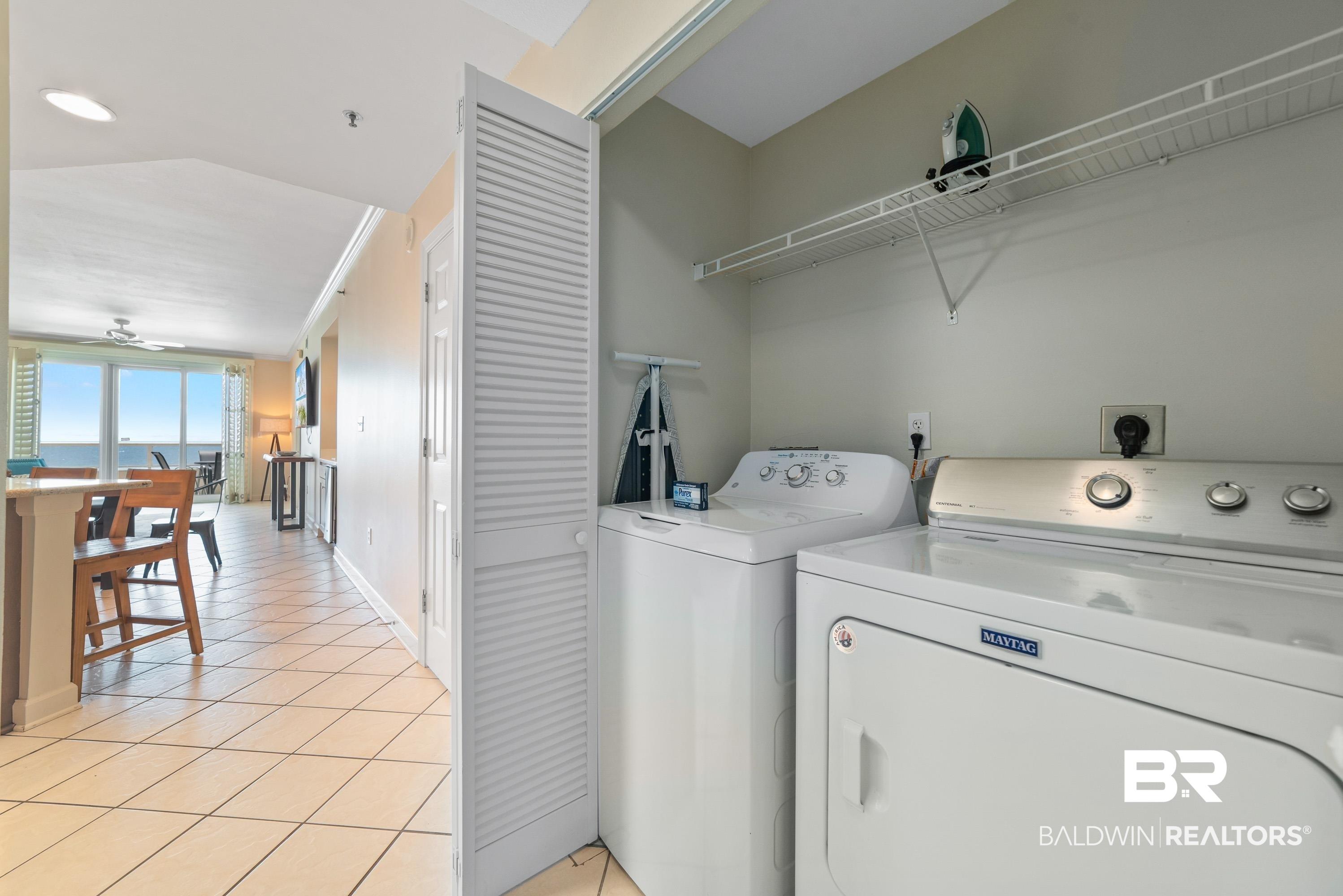Image 2: In-unit laundry appliances with overhead wire shelving, featuring louvered bi-fold doors