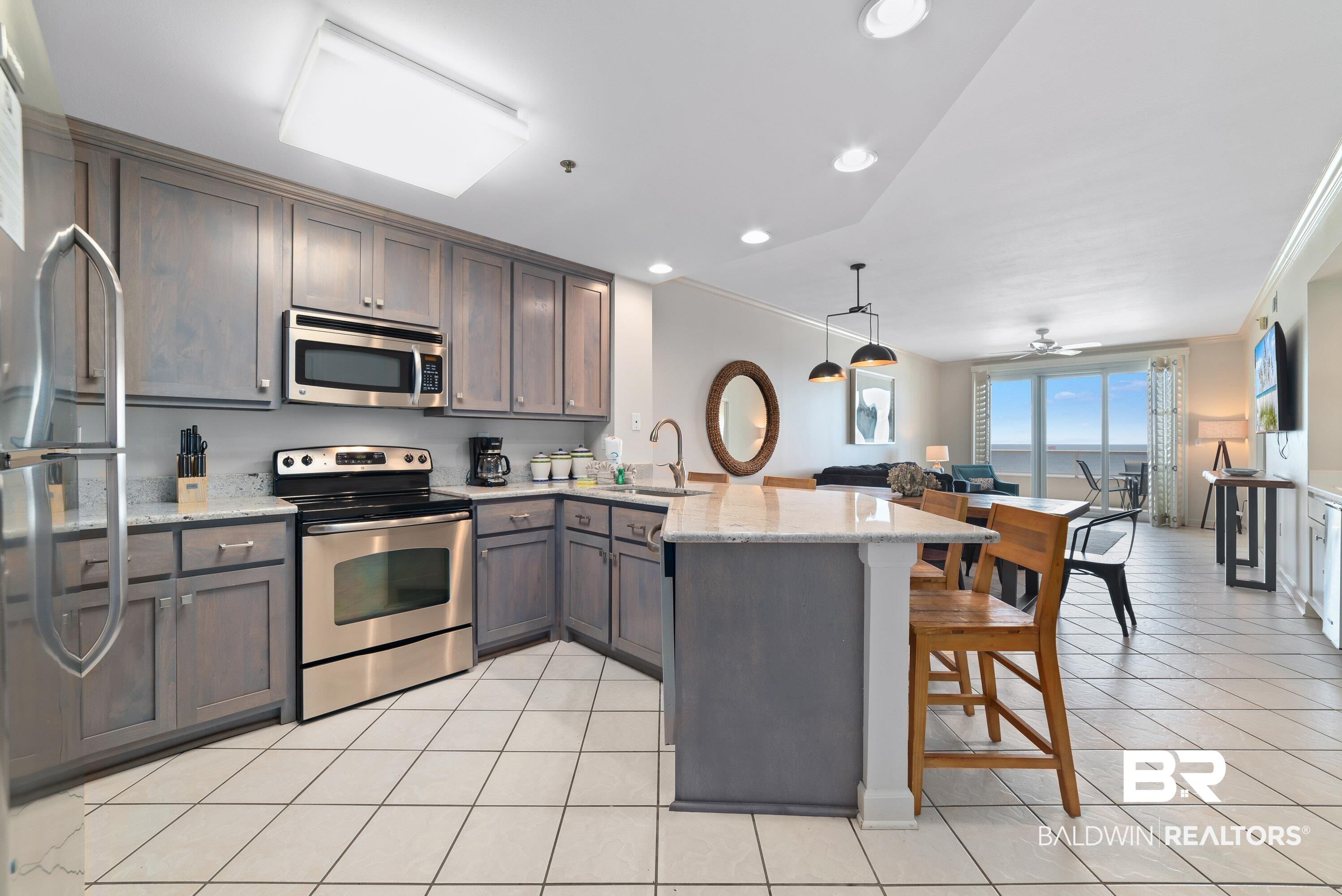 Image 4: Kitchen featuring gray wood-finish cabinetry, stainless steel appliances, and light-toned countertops