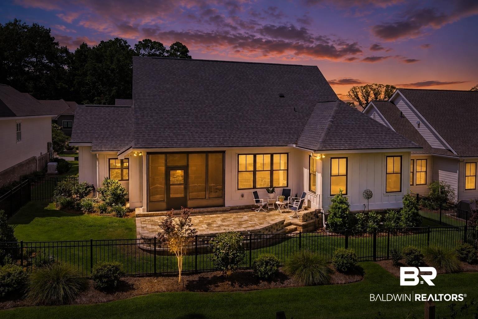 Image 2: Rear exterior featuring a screened porch, paver patio, black metal fencing, and established perimeter landscaping