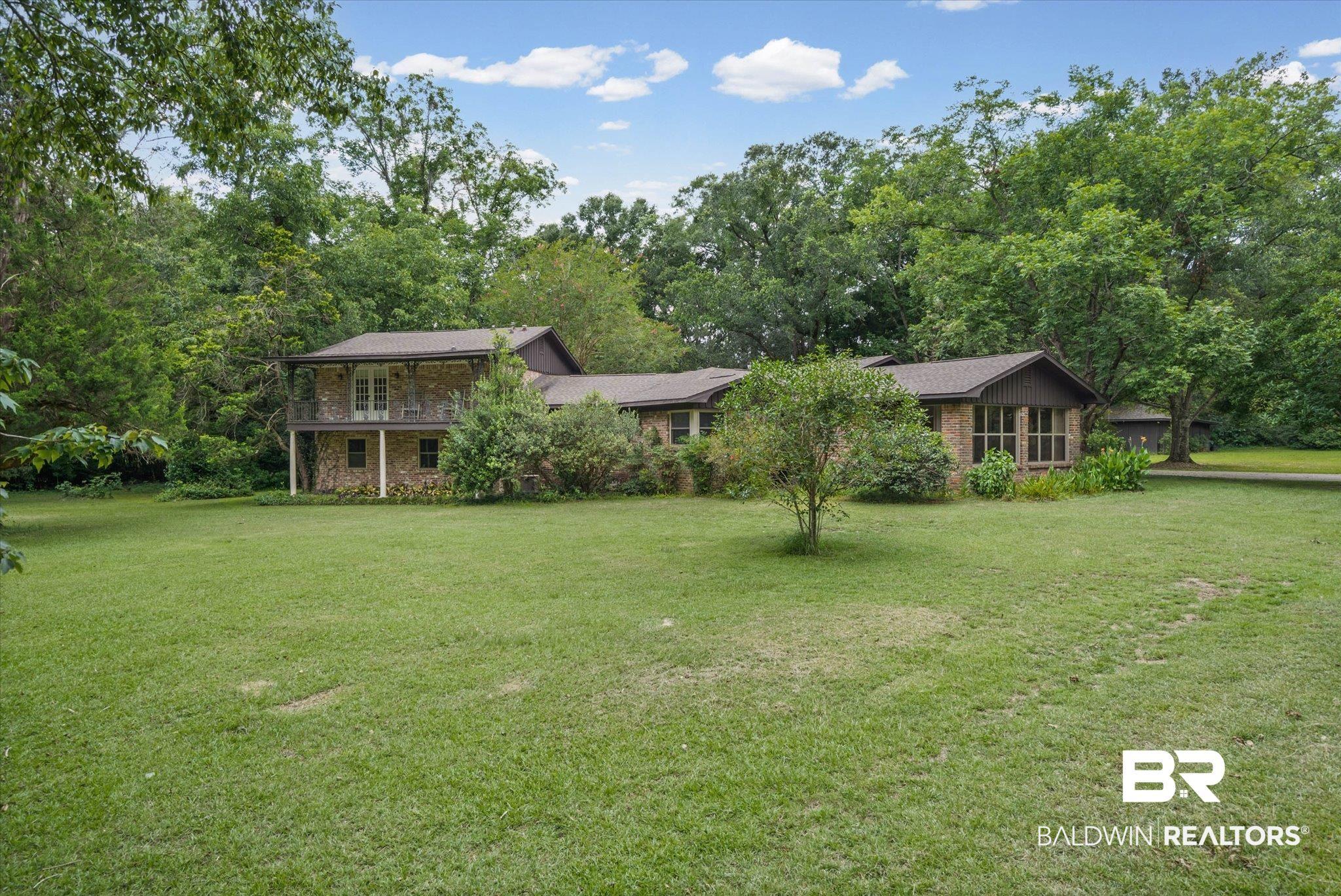 Image 4: Expansive green lawn presenting a stone and wood-sided residence with a covered second-story balcony